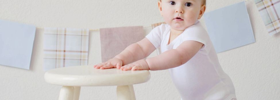 Beispielbild eines Babys, das sich an einem Stuhl festhält und in die Kamera schaut.