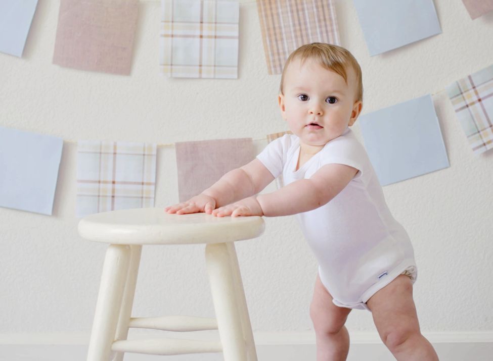 Beispielbild eines Babys, das sich an einem Stuhl festhält und in die Kamera schaut.