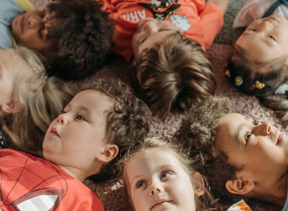 Beispielbild Kindertagespflege mit Kindern, die fröhlich die Beine in die Luft strecken.