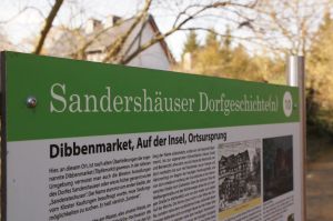 Eine der Infotafeln, die in der Gemeinde verteilt stehen. Hier im Zentrum des alten Ortskerns von Sandershausen.