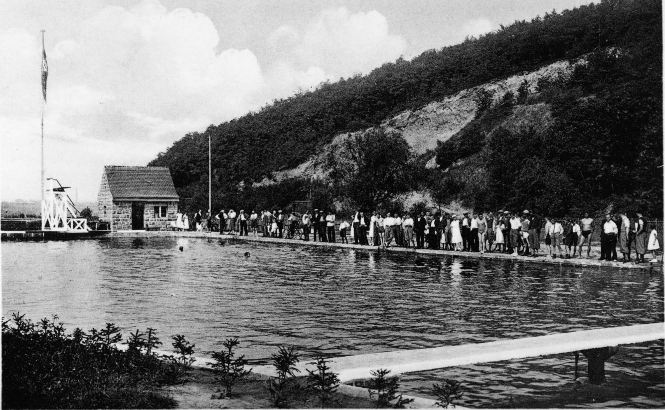 Das Wald-Freibad von Heiligenrode mit dem Hauptbecken und vielen Zuschauern vor der Waldkulisse.