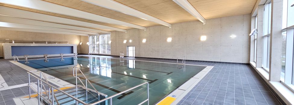 Die Schwimmhalle erstrahlt mit klarem Wasser, einer hellen Holzdecke mit Lichtdurchlässen und einer breiten Glasfront mit Panoramablick auf die Niesteaue.