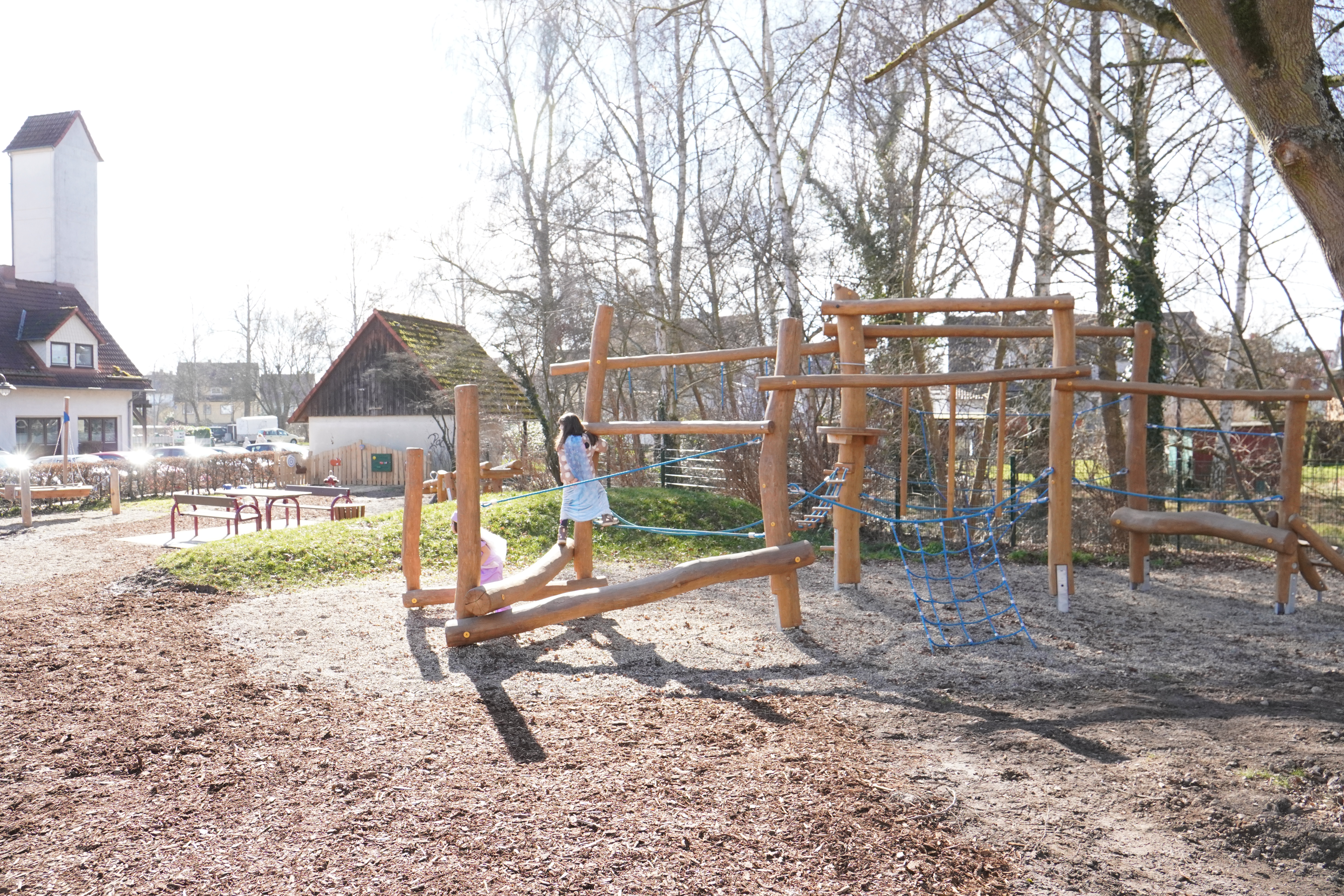 Die Kletterbalken mit Seilen und im Hintergrund die Sandspielfläche und die Boot-Wippe.