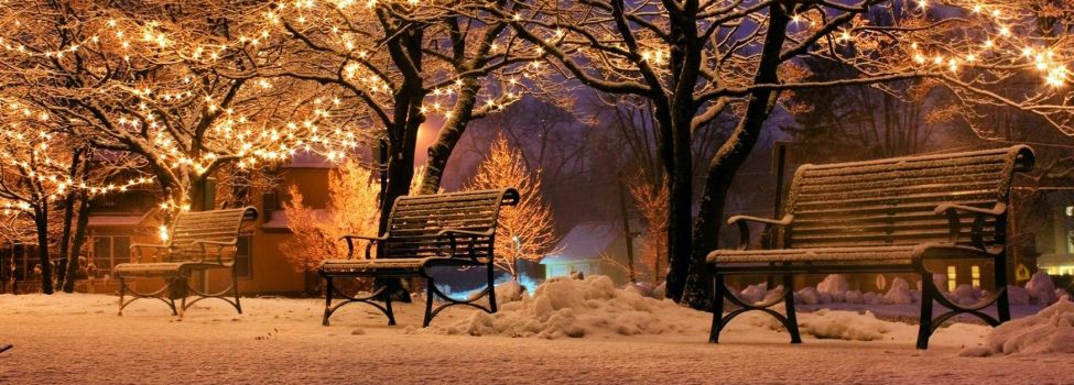 Winterliche Szene mit Bänken und Lichterketten im Park.