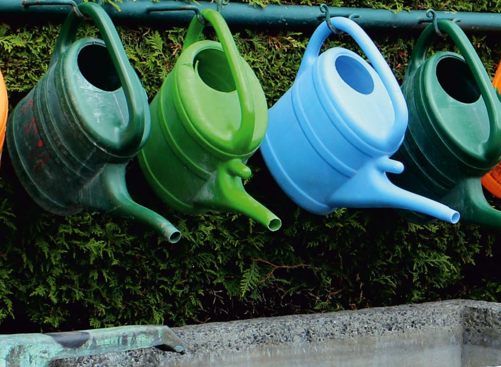 Beispielbild von einem Brunnen am Friedhof und mehreren bunten Gieskannen.
